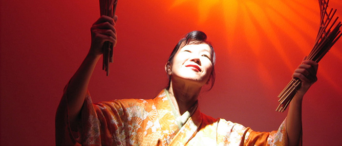 Woman holding bundles of wooden sticks, with an orange sunburst behind her