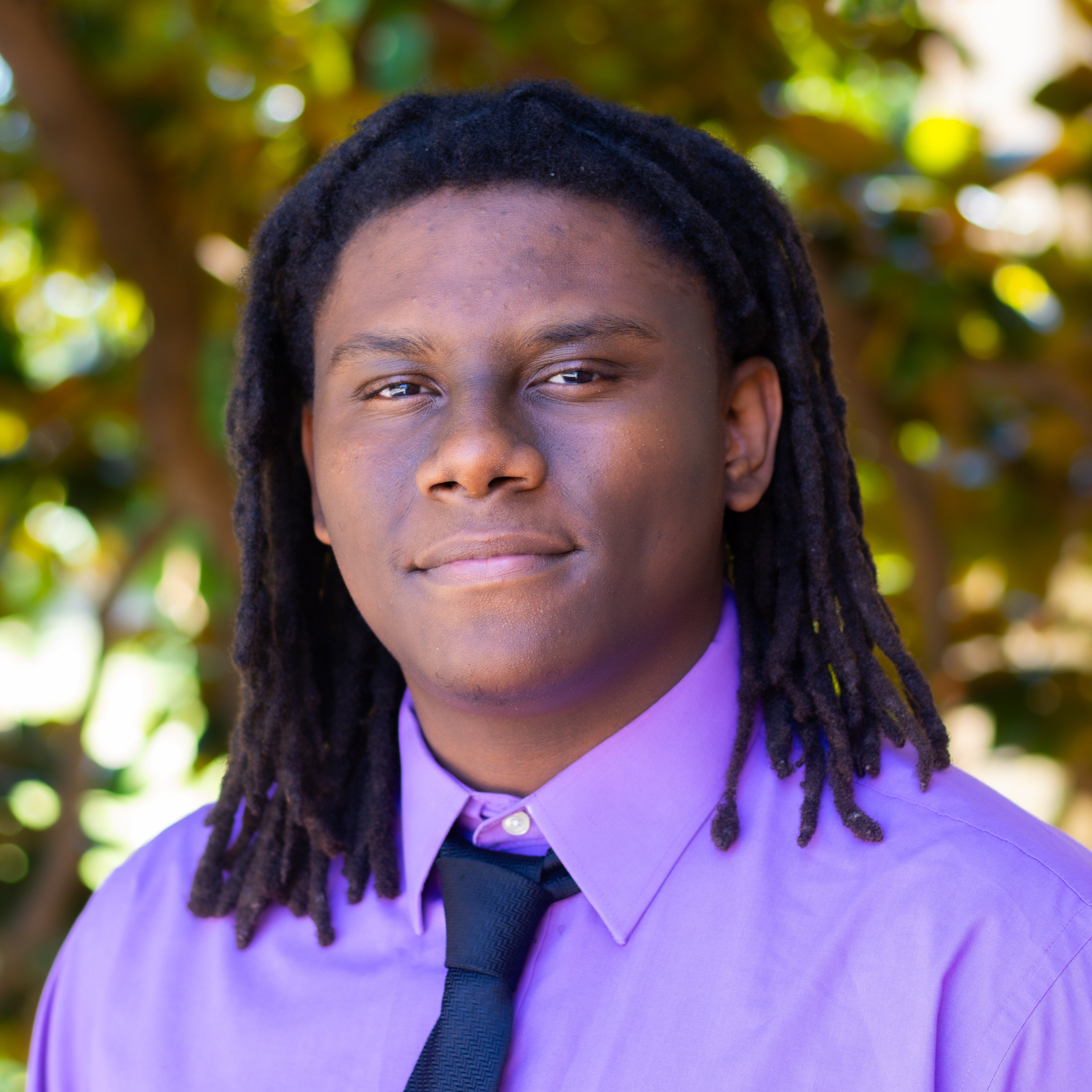 man smiling in purple shirt with navy blue tie and dark hair 