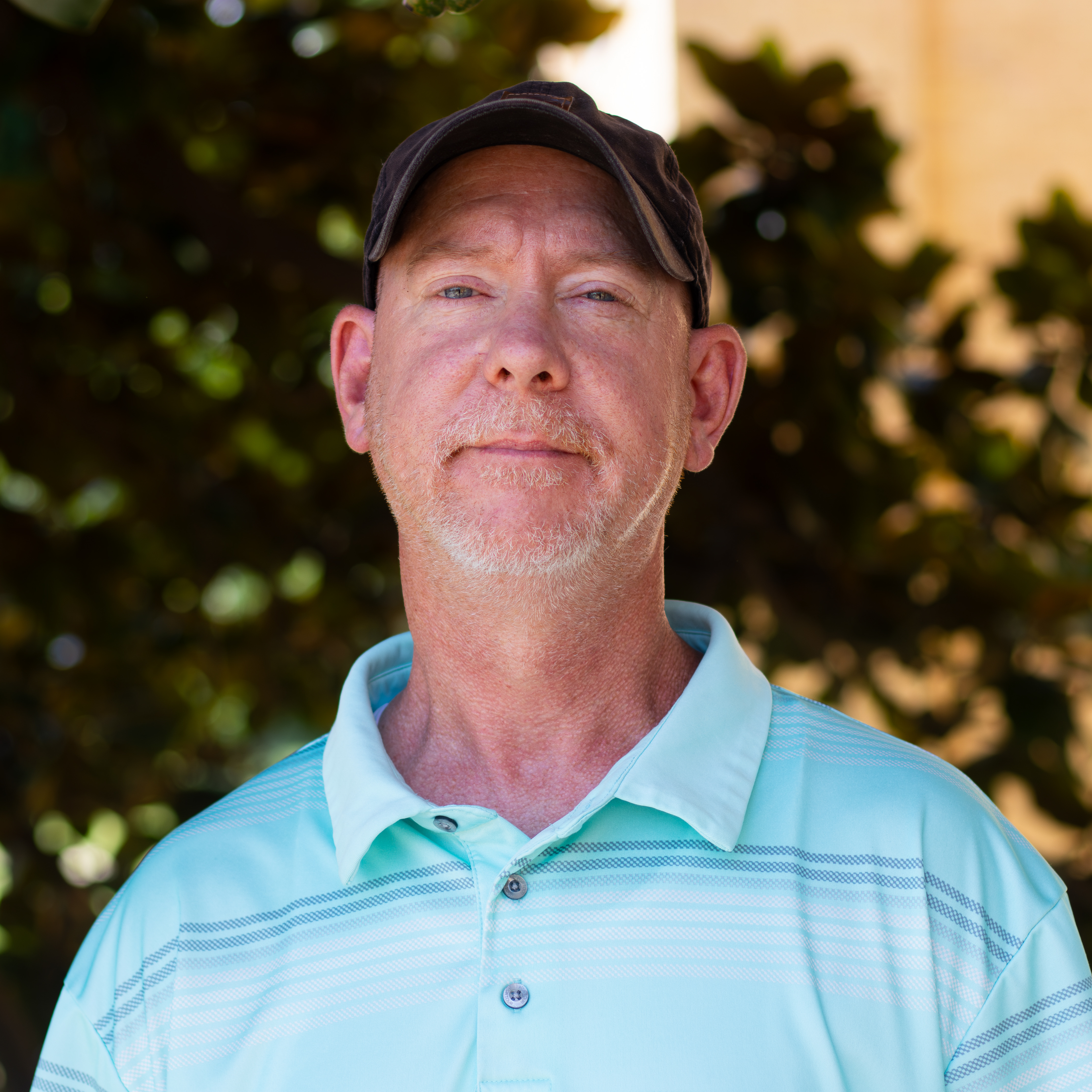 man looking into camera wearing a blue polo and brown baseball cap
