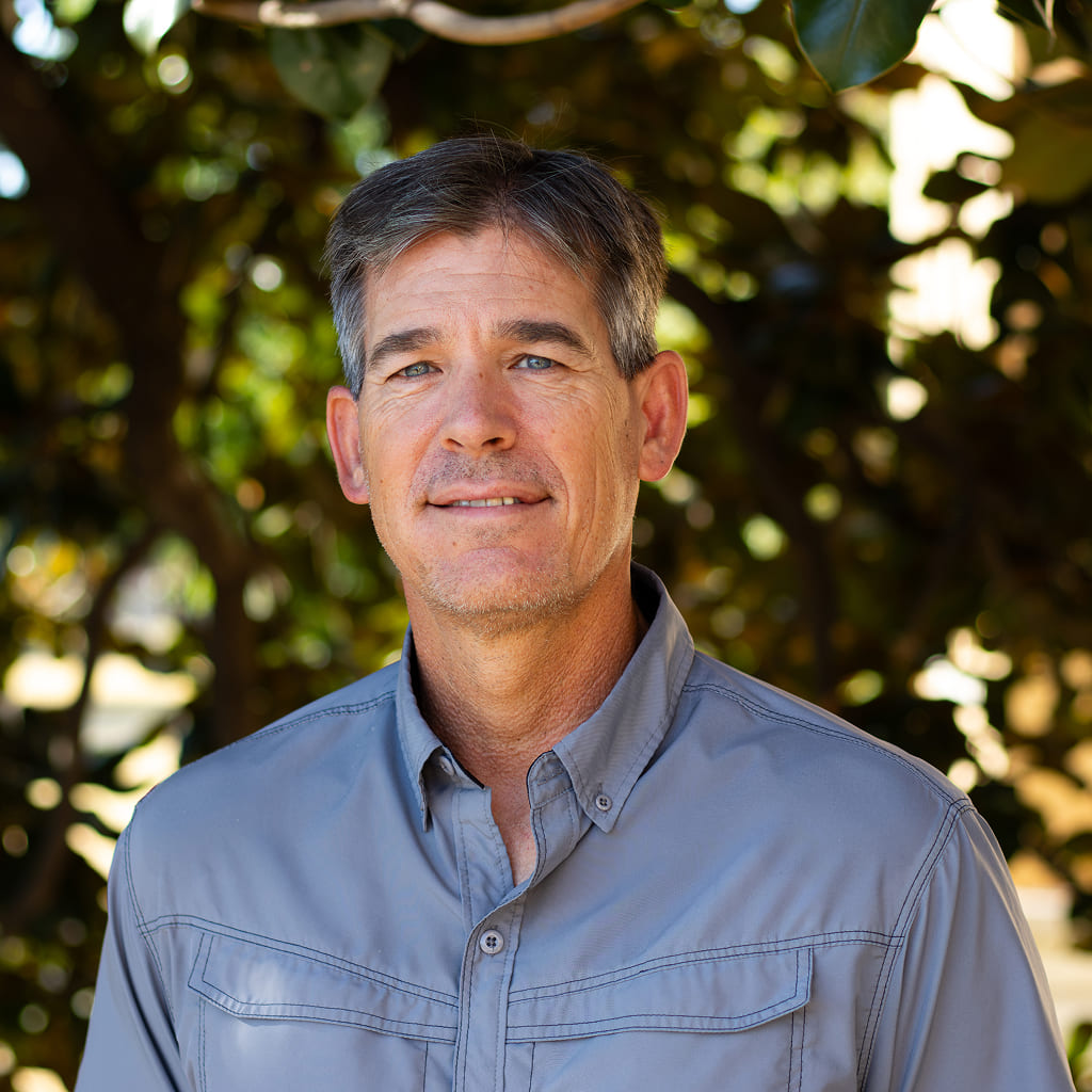 A man in a gray button up shirt standing and smiling